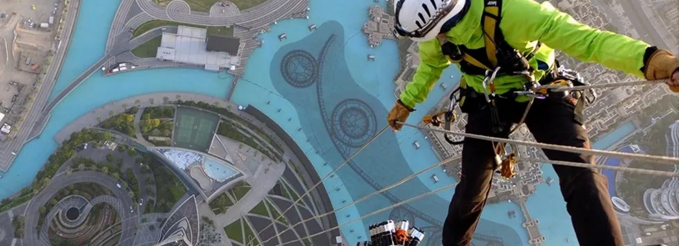 A man abseiling down a building, holding the rope of a colleague