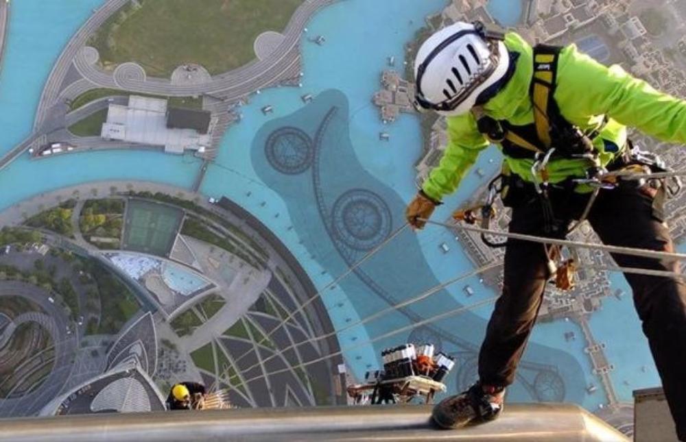 A man abseiling down a building, holding the rope of a colleague