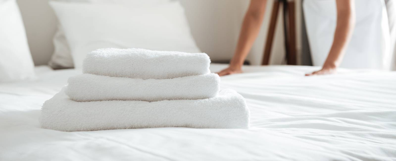 3 white towels on a bed as a maid presses the sheet