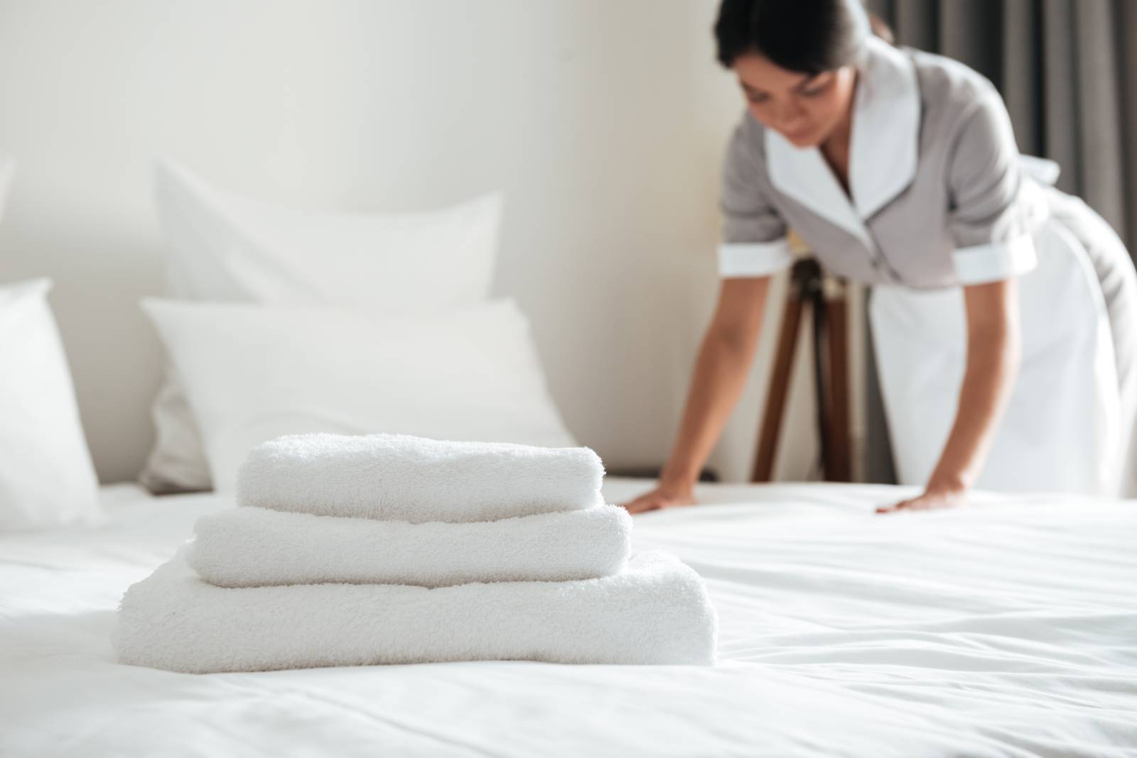 3 white towels on a bed as a maid presses the sheet