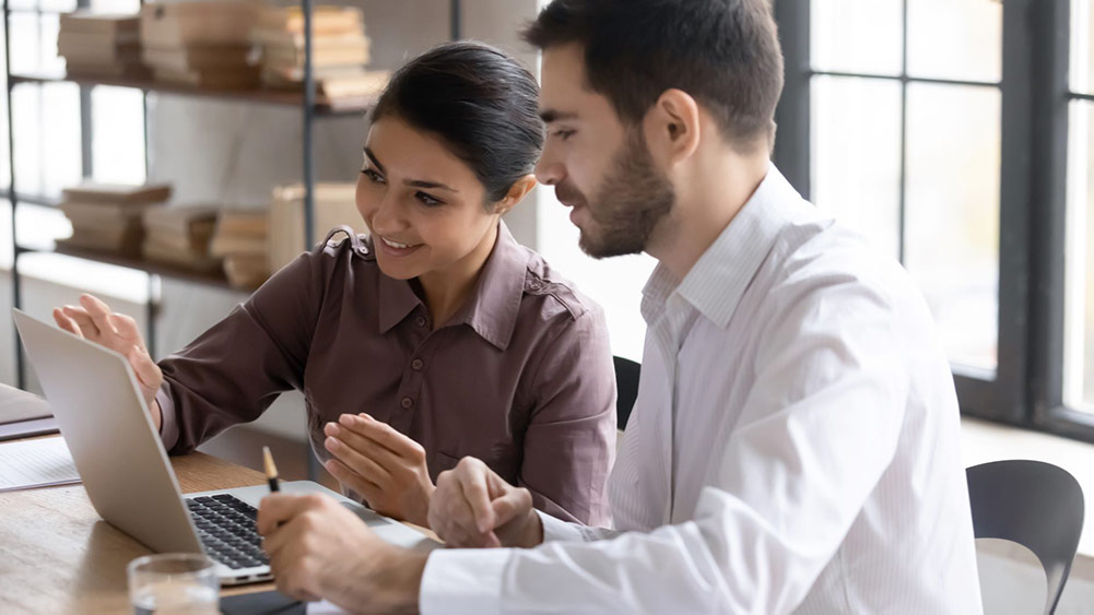 A man and a woman sat pointing in front of a laptop