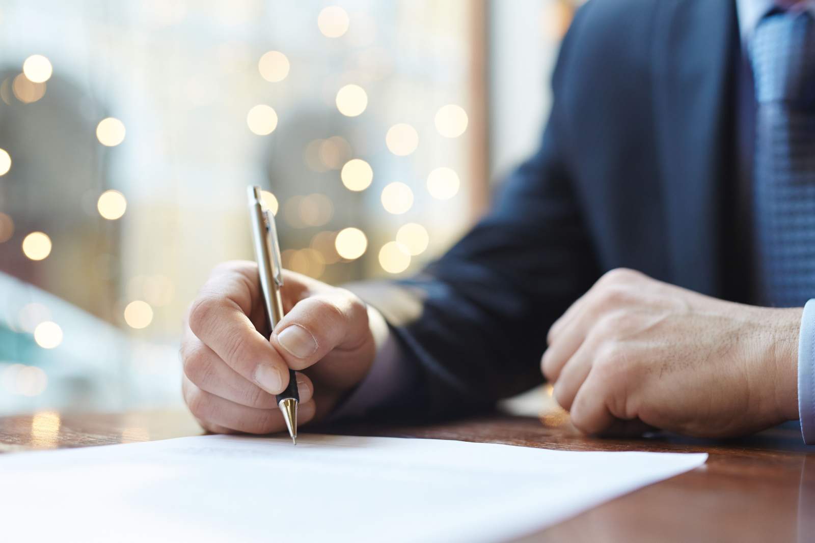 Businessman sat at a desk writing on a document with a gold pen in his right hand