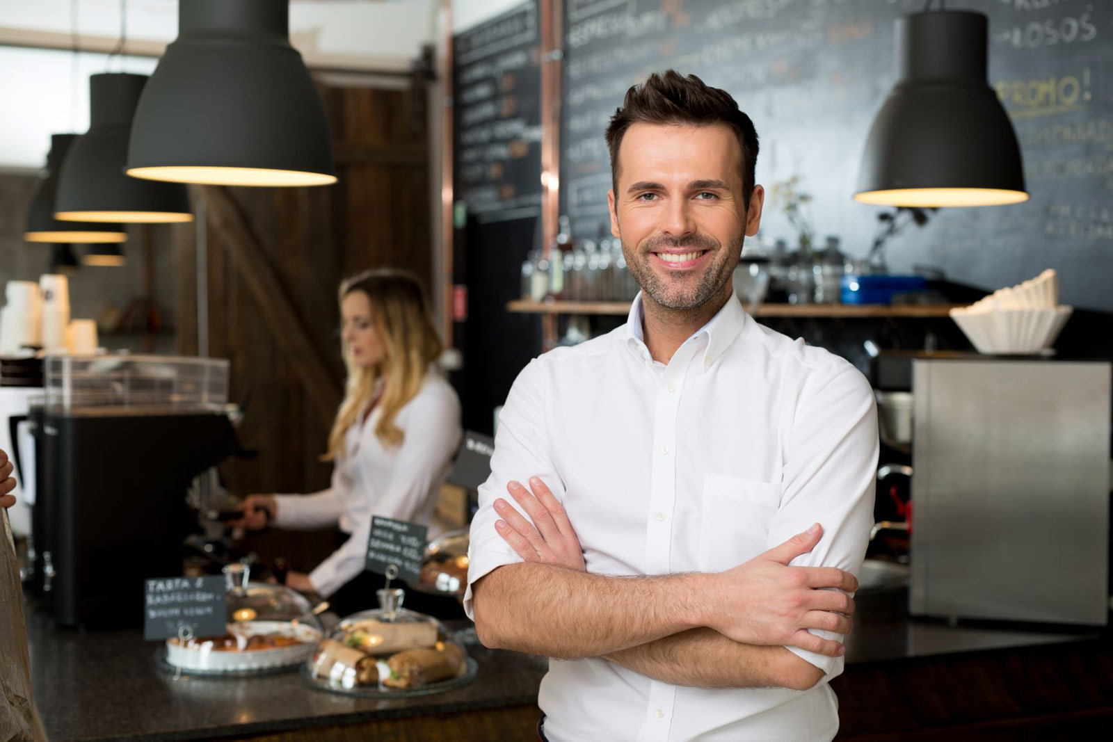 Man in white shirt stood with his arms folded in front of a serving counter 