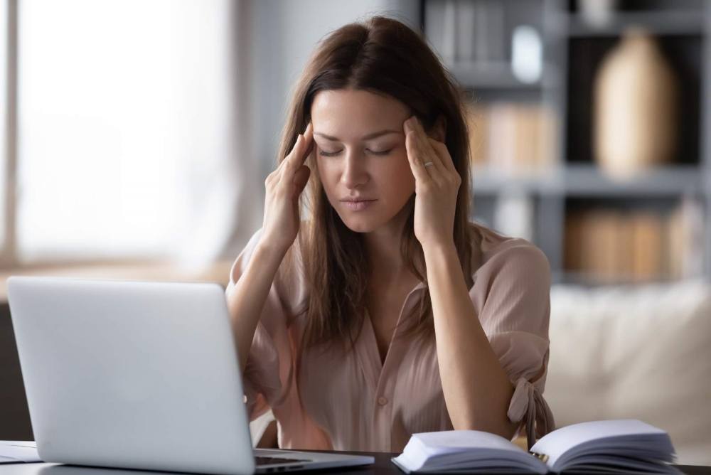 A Woman sat in front of a laptop with her hands on her temples